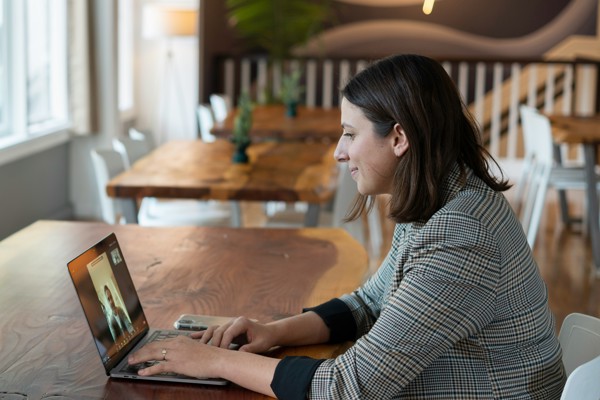 Person sitting at a wooden table in a modern, well-lit room, using a laptop for a video call with someone on the screen, symbolising communication in a long-distance relationship.