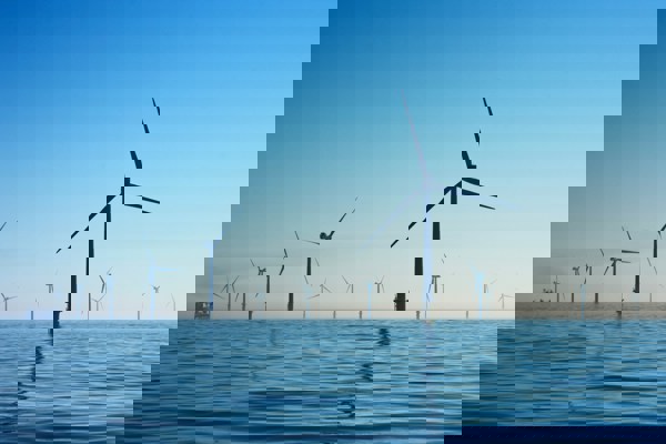 Offshore wind farm with multiple turbines spread across calm ocean waters under a clear blue sky, with a ship visible in the distance on the left.