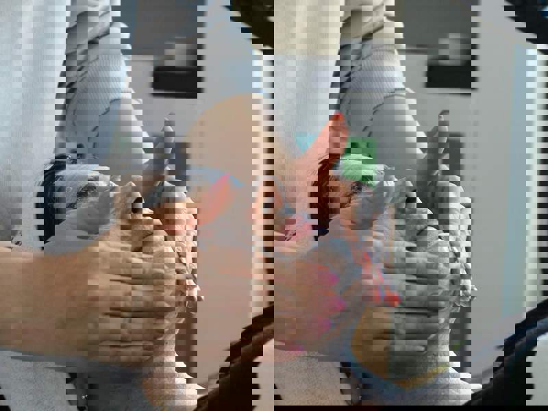 Person receiving a facial treatment while lying down, wearing a white headband, as a practitioner applies a cream or mask to their face. Skincare products are visible on shelves in the background.